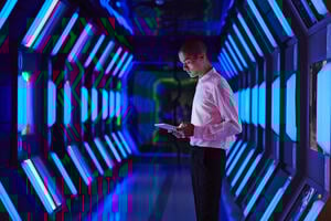 a young man standing with a tablet inside a data warehouse with futuristic lighting
