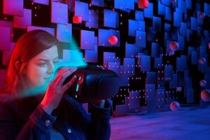Woman looking into a VR headset against a futuristic backdrop of squares and floating circles.